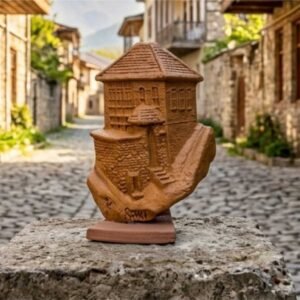 A high-definition front view of the unique 1-of-1 KÜP handcrafted ceramic plate showcasing a detailed 3D relief sculpture of a traditional Sheki house with a red-tiled roof nestled within a rugged mountain landscape on matte raw clay, certified authentic by master Kamran.