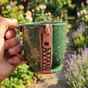 A high-definition front view of the unique 1-of-1 KÜP handcrafted ceramic mug featuring a detailed 3D relief of a lock and key on raw matte clay with a glossy emerald green handle.