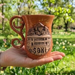 A high-definition handcrafted ceramic mug featuring a highly detailed, hand-sculpted 3D relief of the Sheki Khan’s Palace facade, integrated calligraphic logo for KÜP Ceramics House, with raw matte clay exterior and contrasting deep indigo blue glaze on the handle and interior, certified unique 1 of 1 by master Kamran.