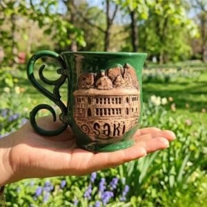 A unique handcrafted 1-of-1 ceramic mug featuring a detailed 3D relief of the Sheki Khan’s Palace facade on raw matte clay, with a contrasting glossy emerald green interior and handle, created by KÜP Ceramics House.
